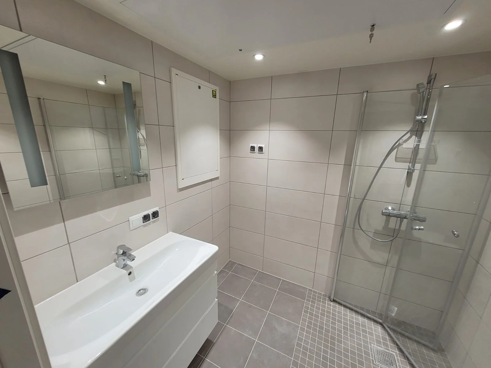 Flislagt baderom med moderne hvit servantskap, speilskap og glassdusj - Badrenovering