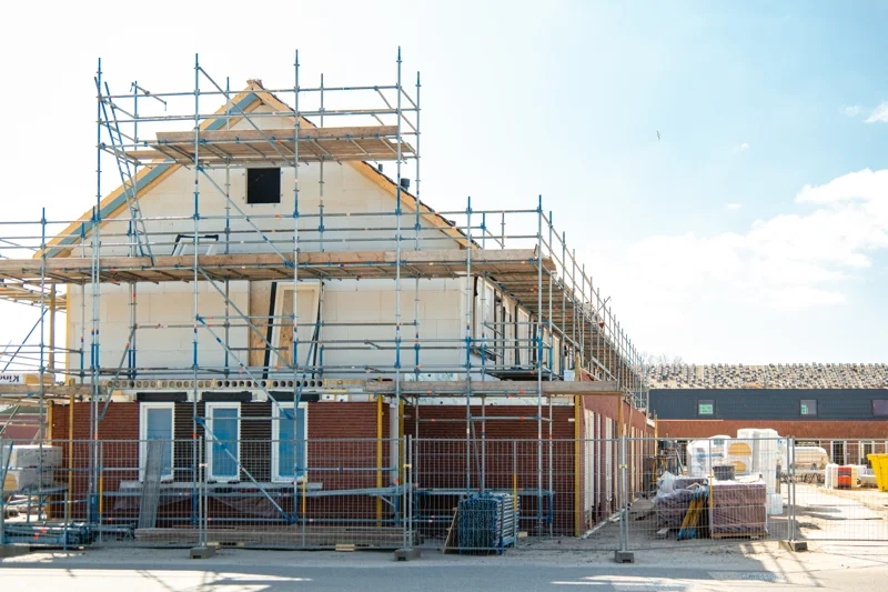 Stillas rundt toetasjes bolig med murvegger og byggeplass foran under renovering av hus